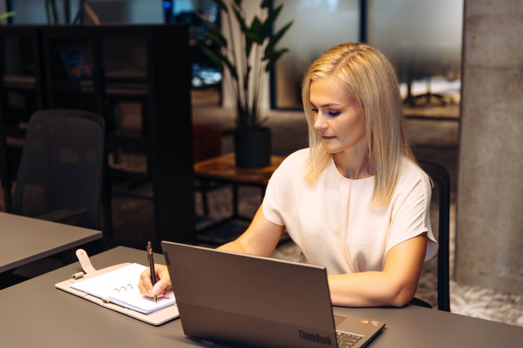 Naine kirjutab käsitsi e-poe tellimuse andmeid ümber, laptop laual